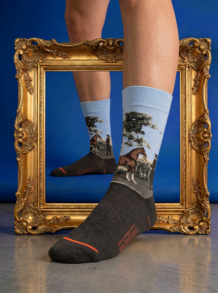 Charcoal grey ArtyGifts socks with pale blue cuffs and horse artwork, styled within an ornate gold frame against a blue background.