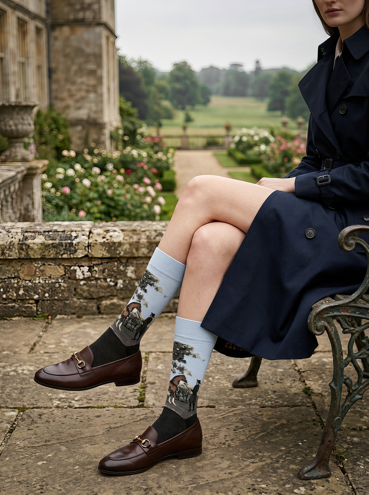 Person seated beside a garden wearing charcoal grey ArtyGifts socks with pale blue cuffs and brown brogue shoes.