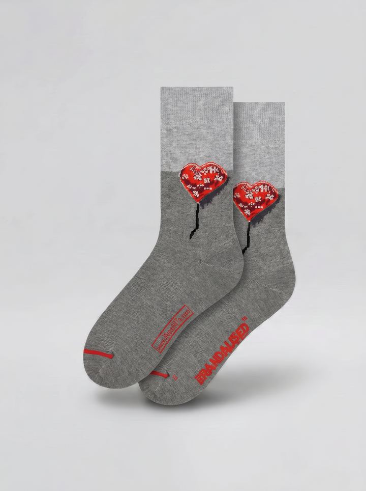 Pair of grey Bandaged Heart art socks featuring red heart motifs, black details and red accents, displayed against a pale grey background.

