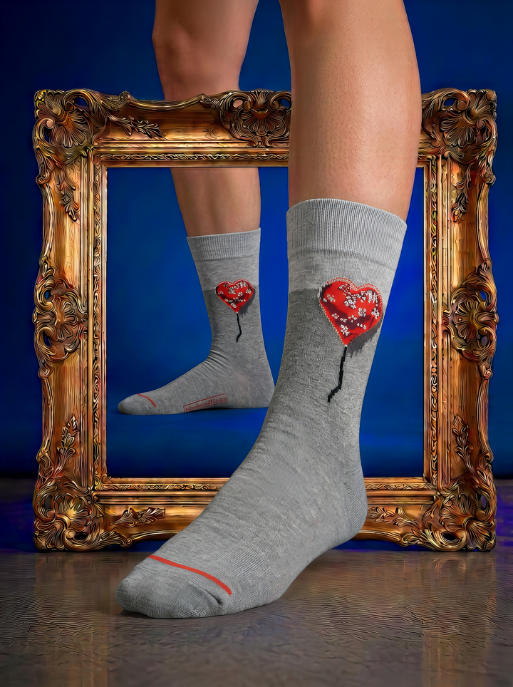 Grey Bandaged Heart art socks with red heart motifs, worn on feet beside an ornate gold frame against a deep blue background.

