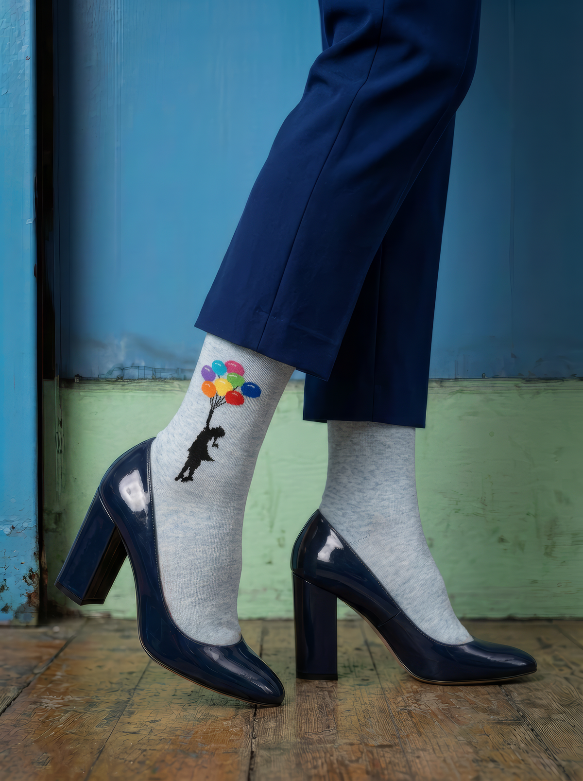 Light grey Banksy-inspired balloon socks styled with cropped blue trousers and pointed black high heels against a teal background.
