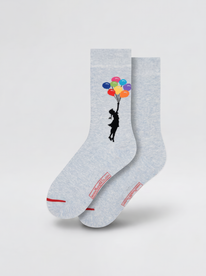 Pair of light grey Banksy-inspired socks with black figures and colourful balloons, displayed against a pale grey background.
