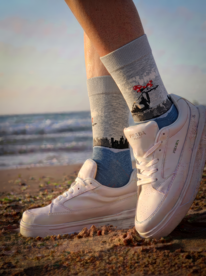 Banksy-inspired Polka Dot Rat art socks worn with white trainers beside the sea in warm sunlight.
