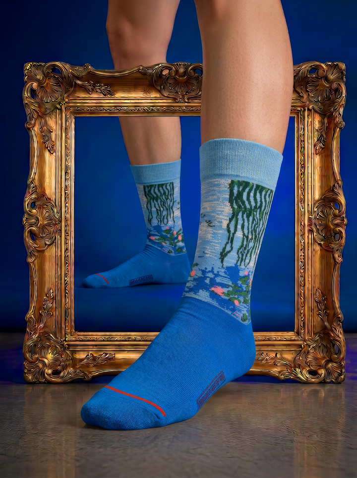 Person wearing blue Claude Monet Water Lilies art socks in front of an ornate gold frame, creating an artistic museum-inspired setting. Unisex art socks for men and women.