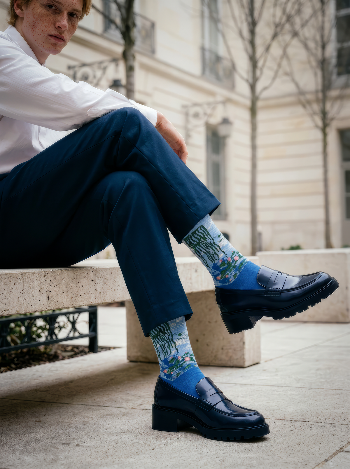 Person wearing blue Claude Monet Water Lilies art socks with dark blue trousers and blue shoes while seated indoors. Unisex art socks suitable for men and women.