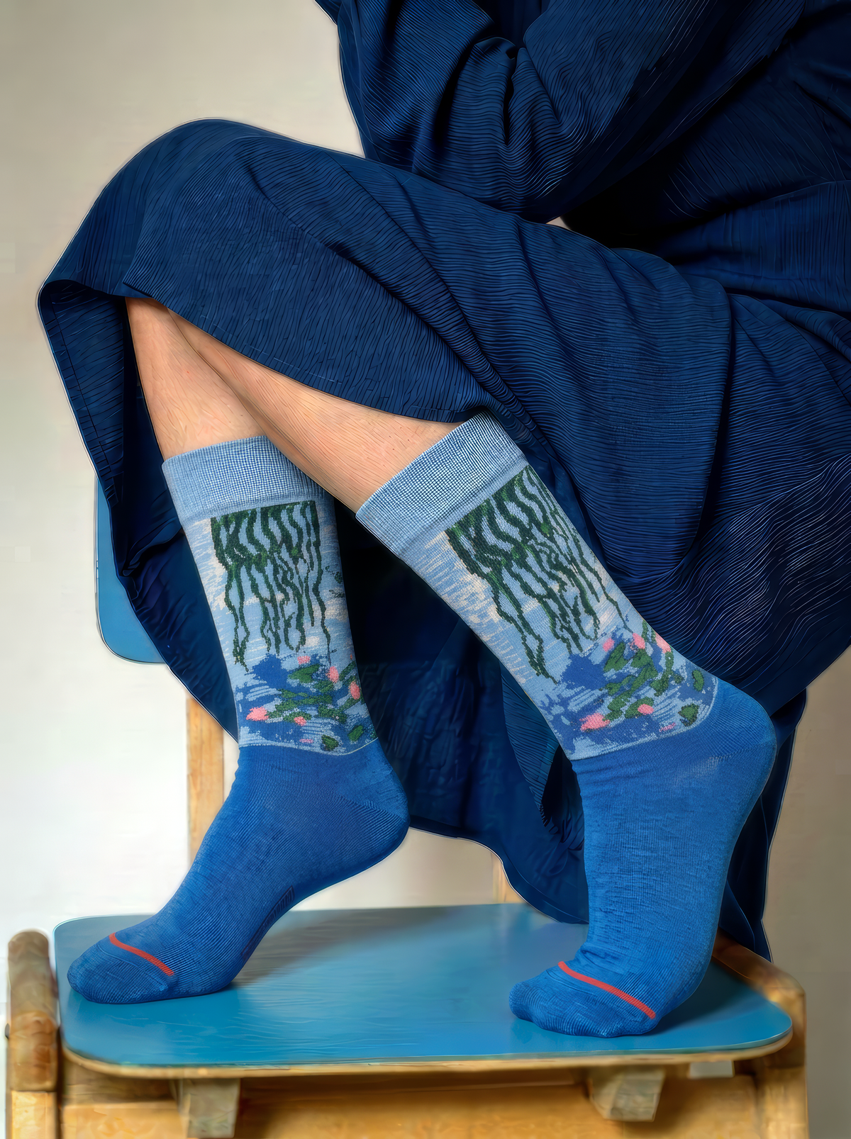 Close-up of blue Claude Monet Water Lilies art socks being adjusted by hand, showing the detailed woven artwork and red toe accent.
