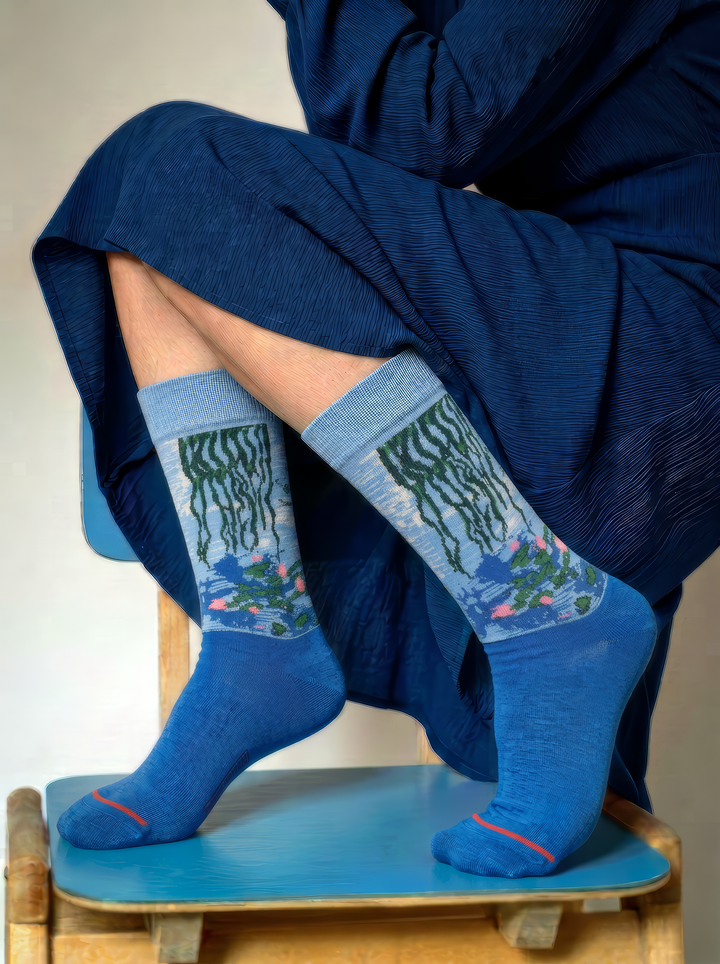 Close-up of blue Claude Monet Water Lilies art socks being adjusted by hand, showing the detailed woven artwork and red toe accent.