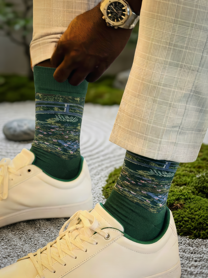 Close-up of a green Claude Monet The Japanese Bridge art sock worn with white trousers, showing the woven artwork and ribbed cuff. For women and men.
