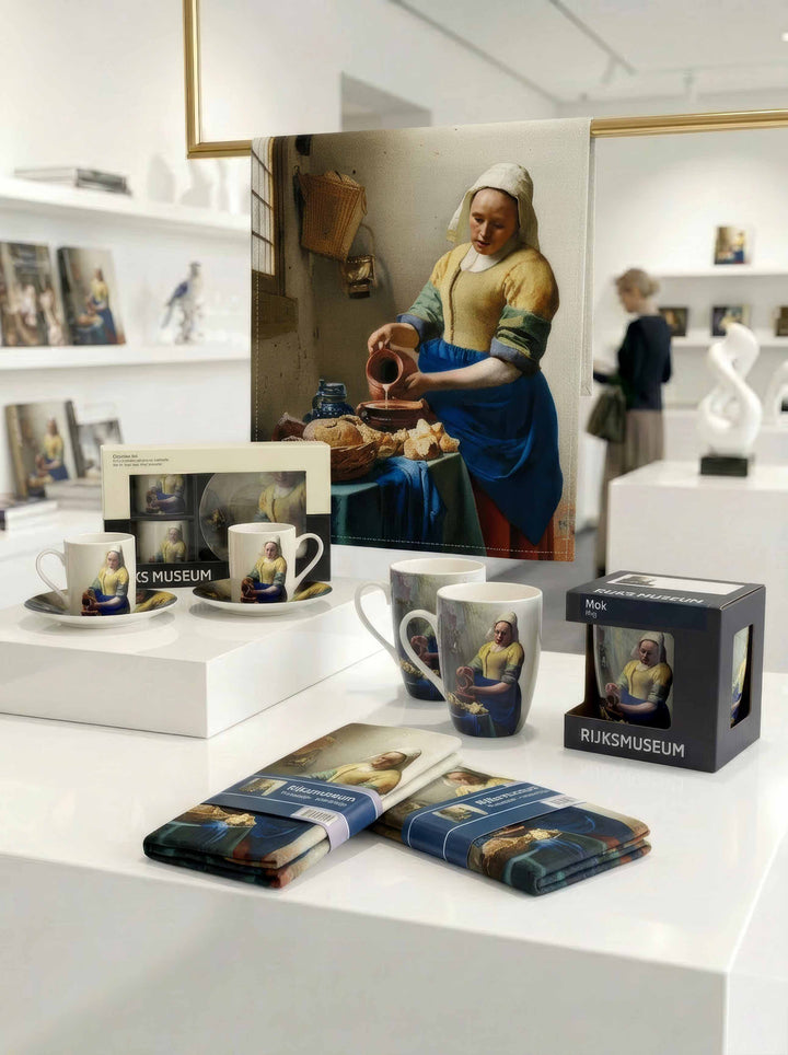 The Milkmaid coffee and tea gift set collection by Johannes Vermeer displayed in Rijksmuseum shop — mug, espresso set and tea towels with museum visitor in background | ArtyGifts
