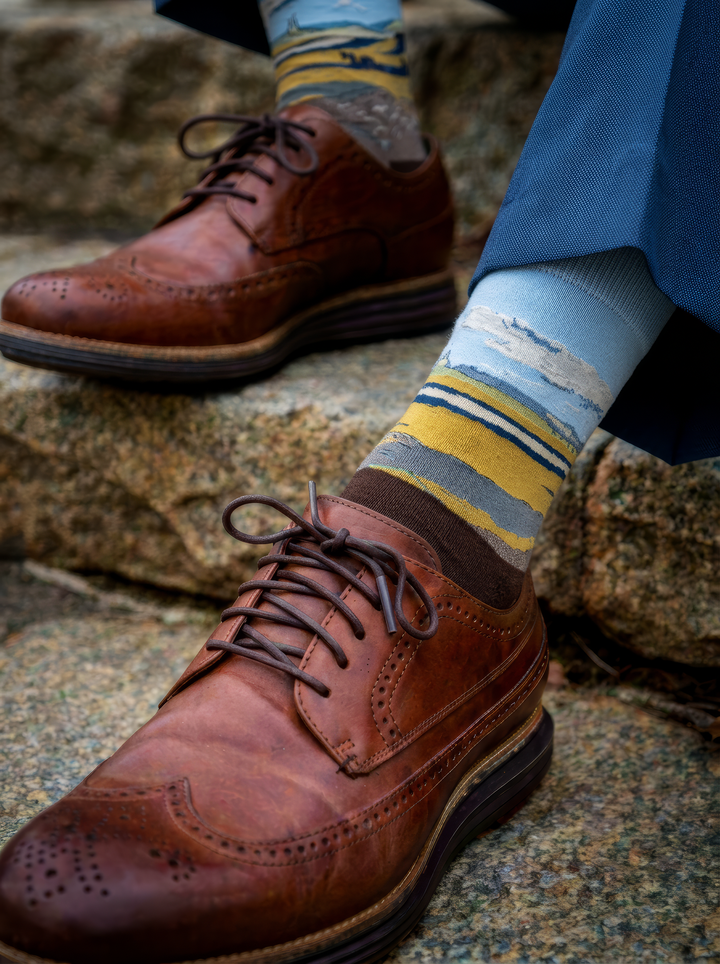 Fenced Field with Ploughman art socks by Vincent van Gogh worn with brown leather brogue shoes and blue trousers on stone steps