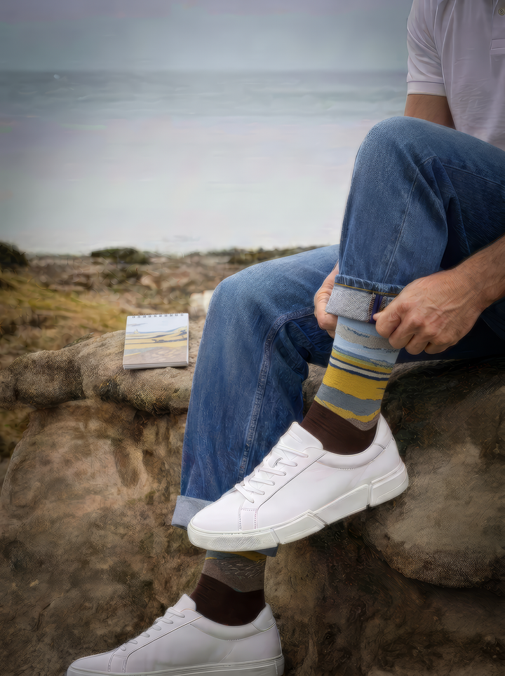 Fenced Field with Ploughman art socks by Vincent van Gogh worn with white lace-up sneakers and blue jeans by the coast