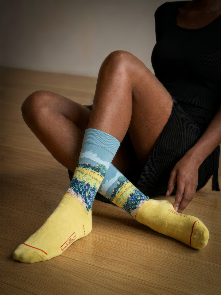 Person wearing yellow Field with Irises at Arles art socks while seated on a wooden floor