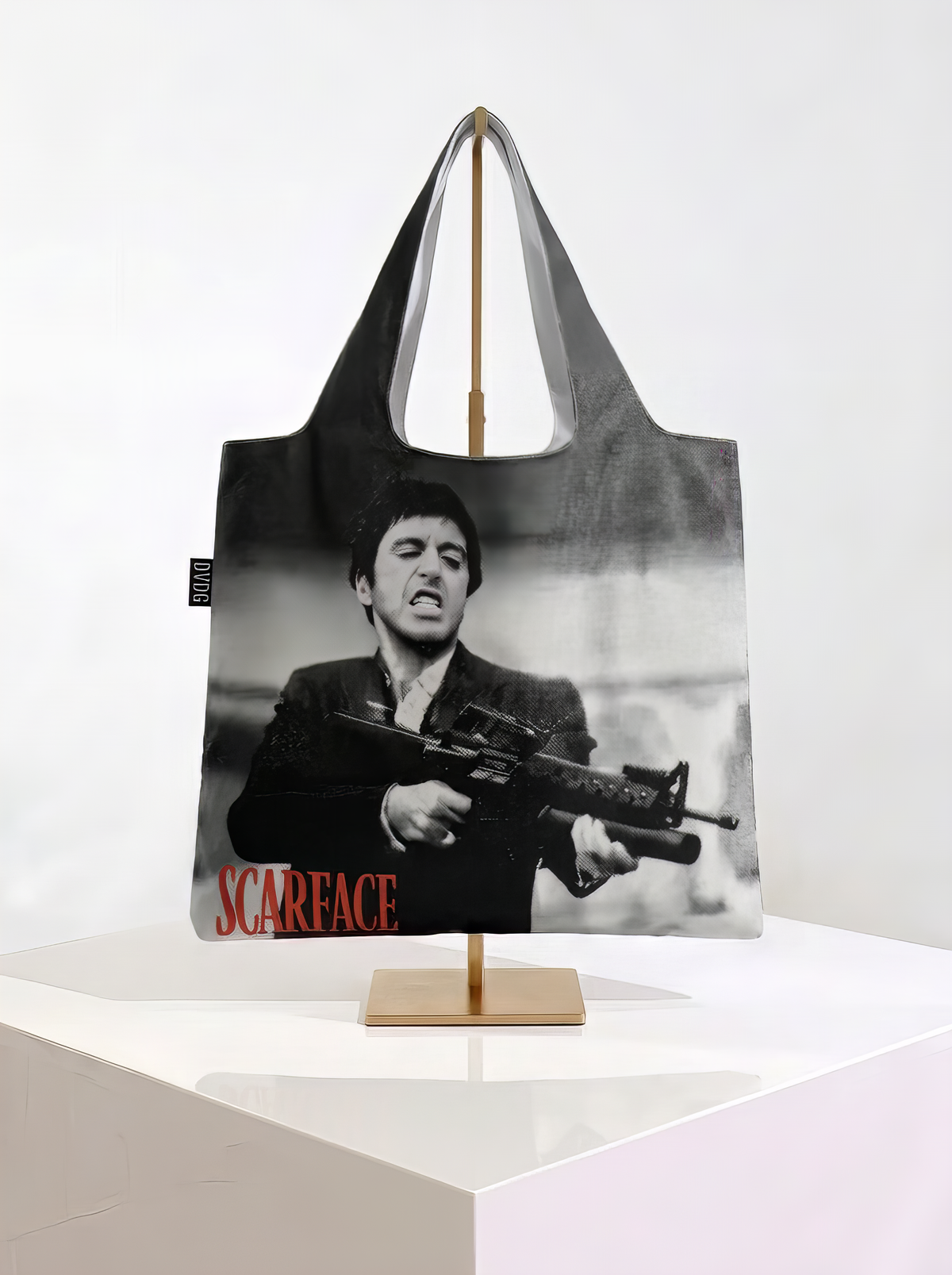 Foldable museum art shopper bag featuring the Scarface design, displayed on a gold stand against a white museum-style background from ArtyGifts
