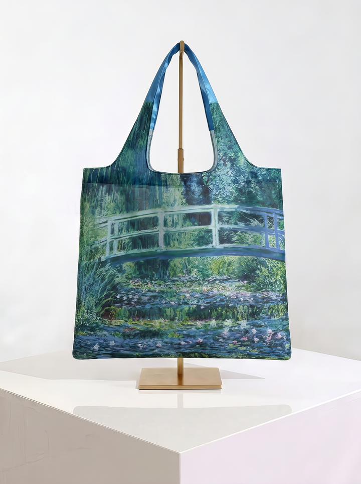 Foldable museum art shopper bag featuring The Japanese Bridge by Claude Monet, displayed on a gold stand against a white museum-style background from ArtyGifts
