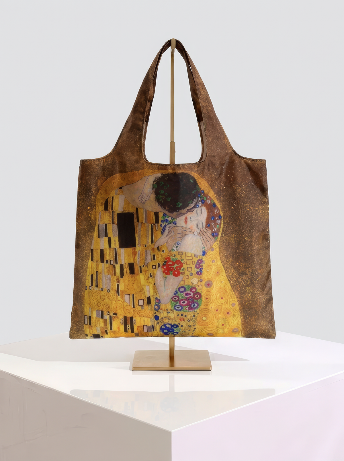Foldable museum art shopper bag featuring The Kiss by Gustav Klimt, displayed on a gold stand against a white museum-style background from ArtyGifts
