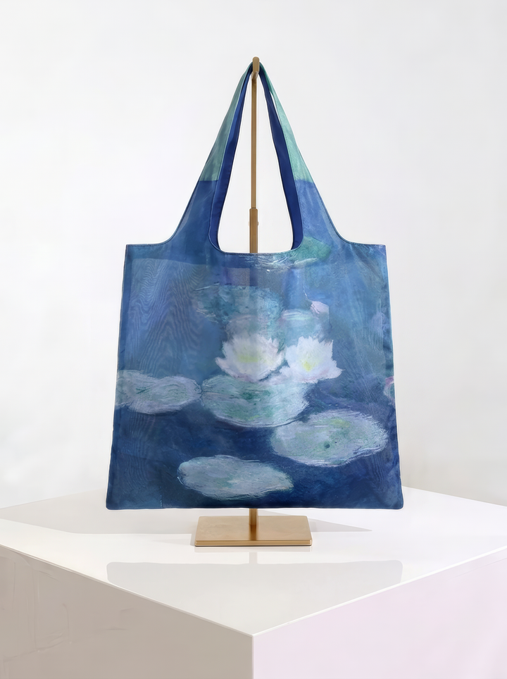 Foldable museum art shopper bag featuring Water Lilies in Evening Light by Claude Monet, displayed on a gold stand against a white museum-style background from ArtyGifts
