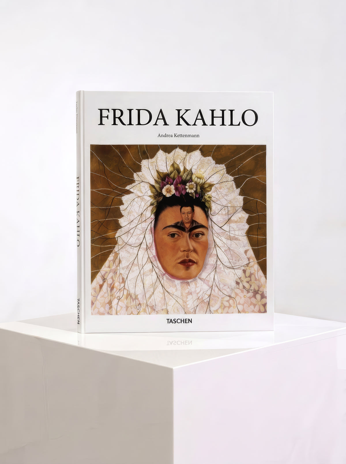 TASCHEN Frida Kahlo hardcover art book by Andrea Kettenmann, featuring a self-portrait in a white Tehuana headdress on the cover, displayed on a white plinth.

