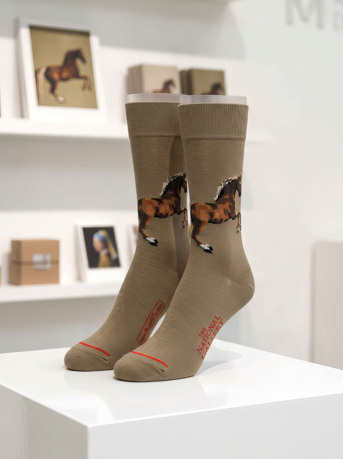 Pair of taupe art socks from ArtyGifts featuring George Stubbs’s horse artwork, displayed on a white pedestal in a museum shop.