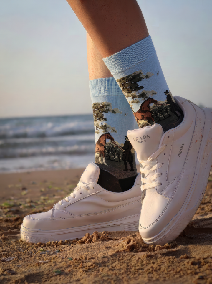 Person by the coast wearing charcoal grey ArtyGifts socks with pale blue cuffs and white sneakers.