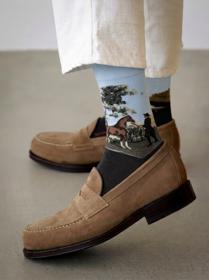 Close-up of an ArtyGifts sock with a charcoal grey foot and pale blue cuff, featuring George Stubbs horse artwork, styled with cream trousers and tan suede loafers.
