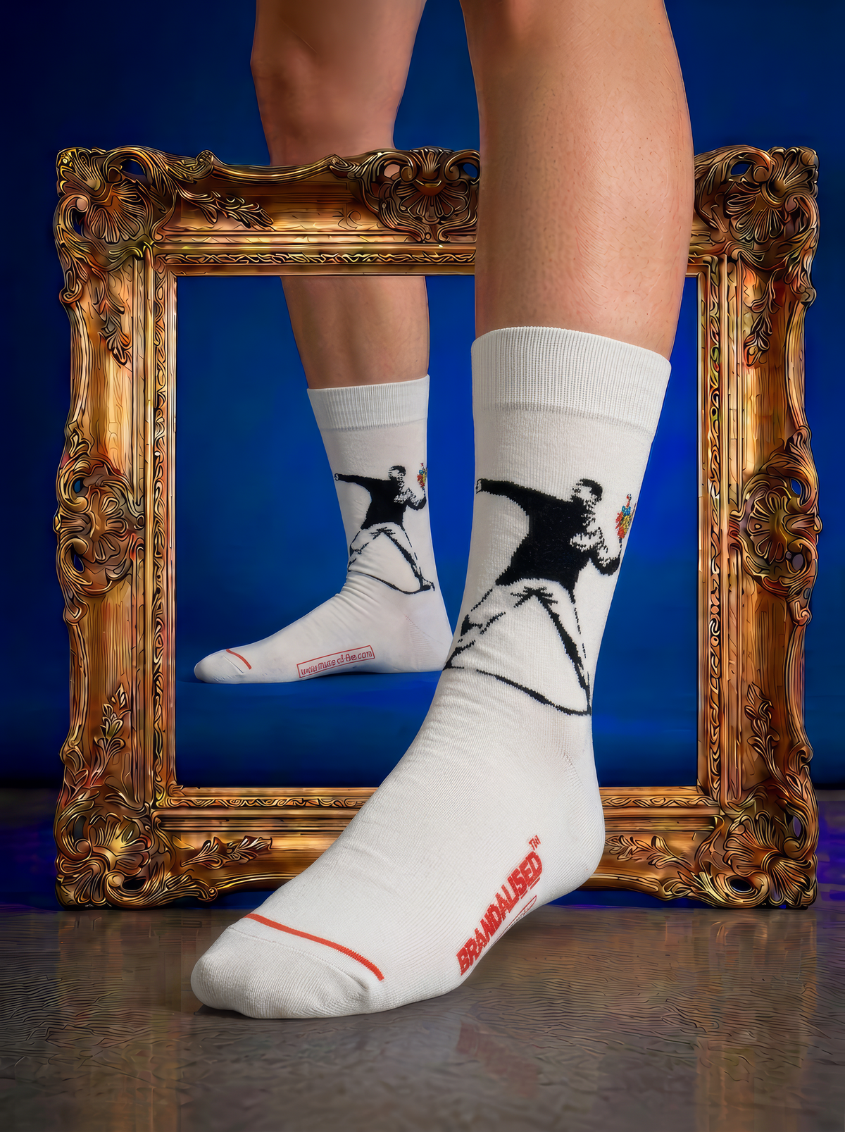 White Love Is in the Air XL art sock, inspired by Banksy, worn beside an ornate gold frame against a blue background.
