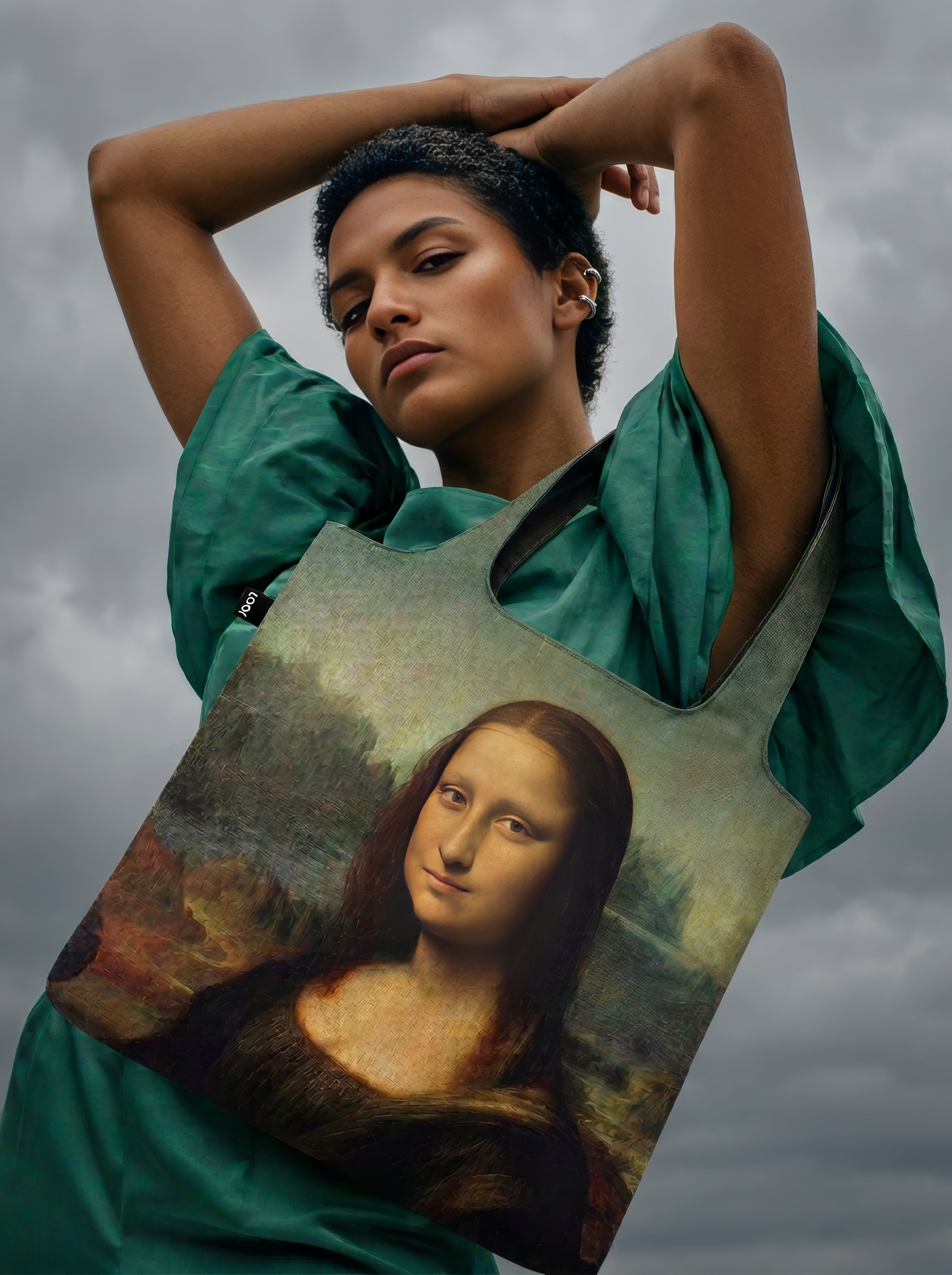 Mona Lisa foldable shopper bag worn by model against dramatic cloudy sky – Leonardo da Vinci art tote from ArtyGifts

