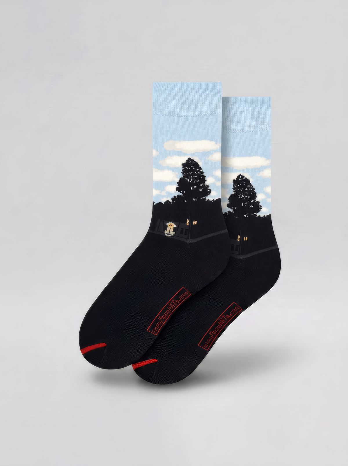Pair of black art socks with pale blue cuffs, white clouds and dark silhouettes, displayed against a light grey background.
