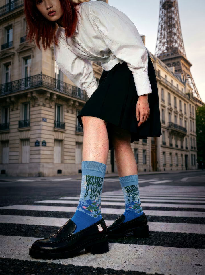 Person wearing officially licensed blue Claude Monet Water Lilies art socks with a white blouse, black skirt and black platform loafers while crossing a Paris street near the Eiffel Tower. Unisex art socks for men and women, suitable as a stylish gift for art lovers.