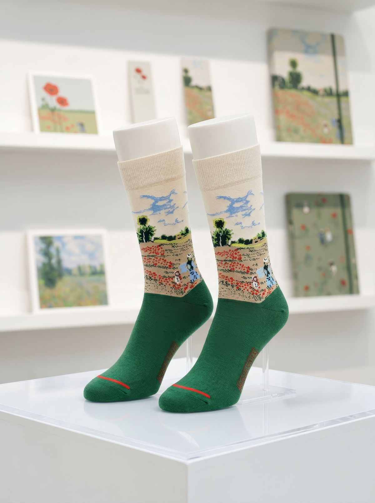 Pair of officially licensed green Claude Monet Field with Poppies art socks displayed on a white pedestal in a bright gallery setting. Unisex art gift for women and men.
