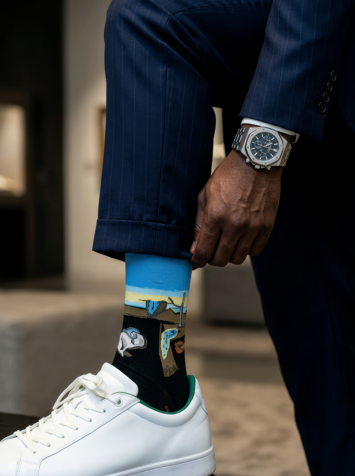 Close-up of a person lifting a navy trouser cuff to show a black XL sock featuring colourful Salvador Dalí artwork, paired with a white sneaker.⠋

