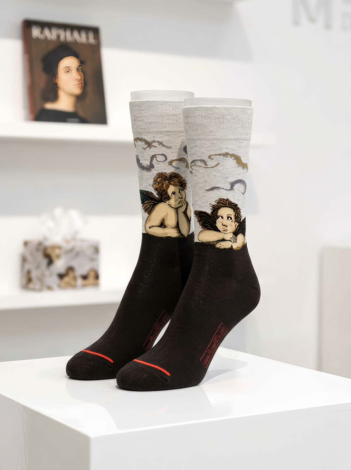 Black Sistine Madonna Angels art socks featuring Raphael’s artwork displayed on a white pedestal