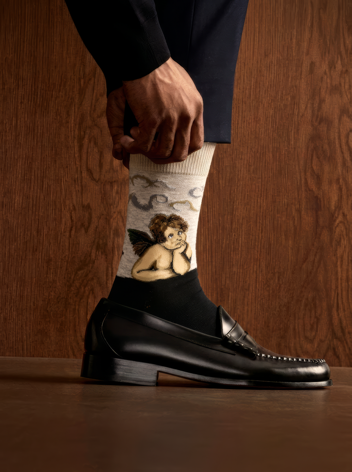 Sistine Madonna Angels art socks featuring Raphael’s artwork worn with a black leather loafer against a wooden background