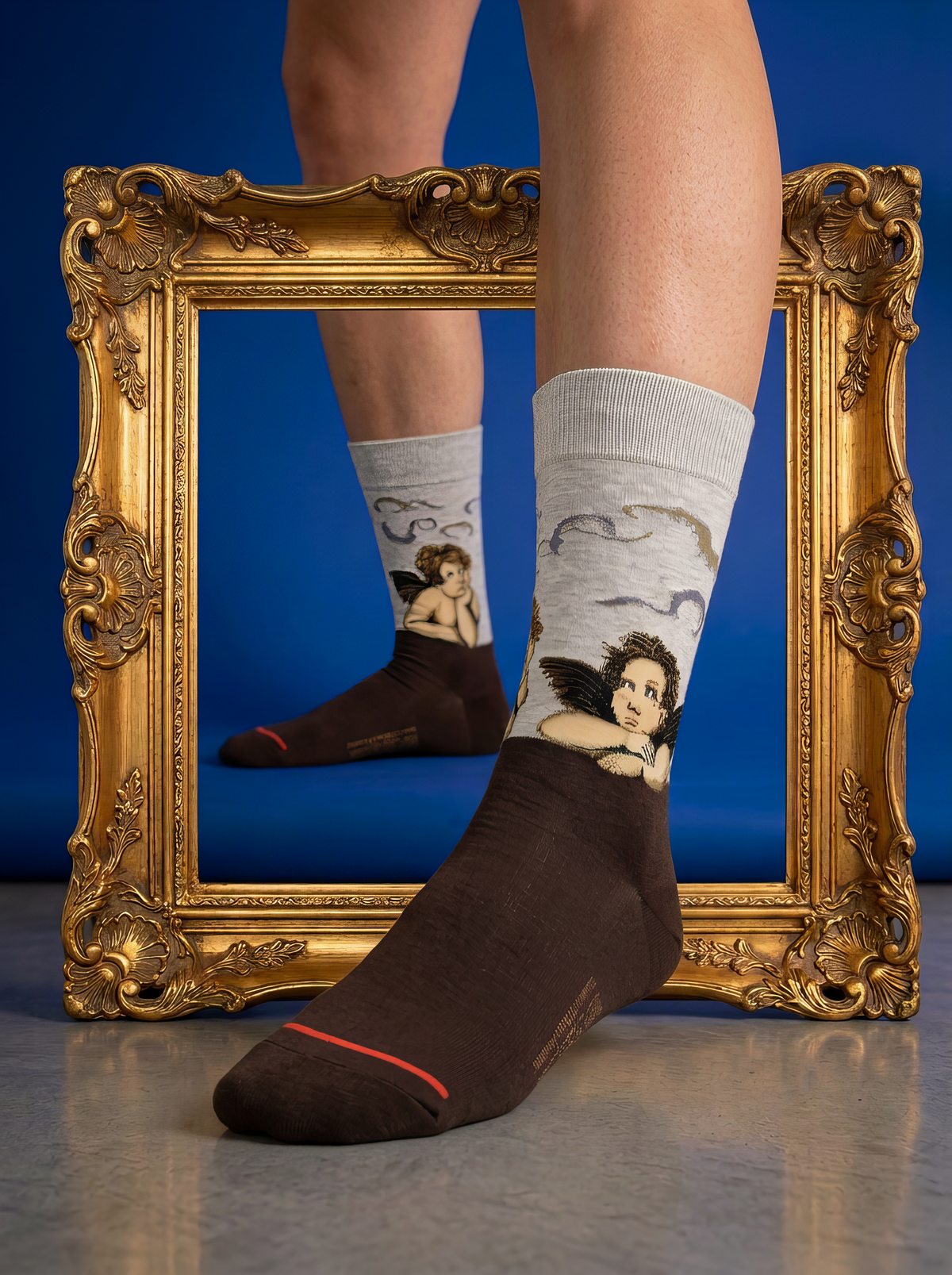 Sistine Madonna Angels art socks featuring Raphael’s artwork worn with a brown leather loafer in front of a gold frame