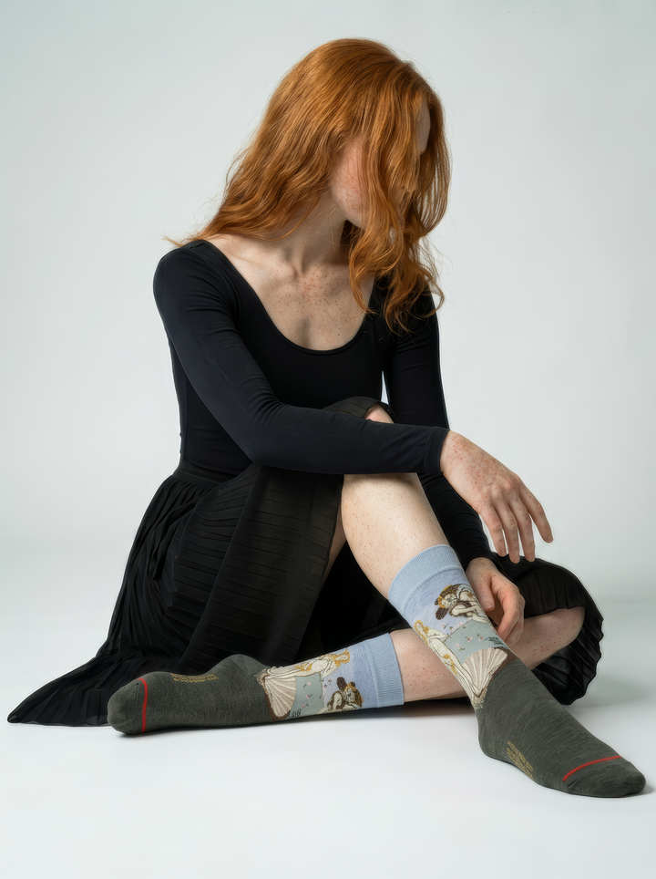 Person wearing The Birth of Venus art socks featuring Botticelli’s artwork without shoes in a seated pose