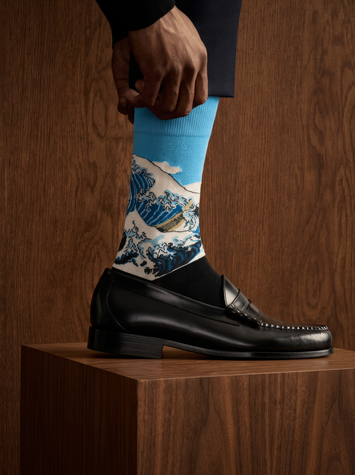 The Great Wave Blue art socks by Katsushika Hokusai worn with a black leather loafer against a wooden background