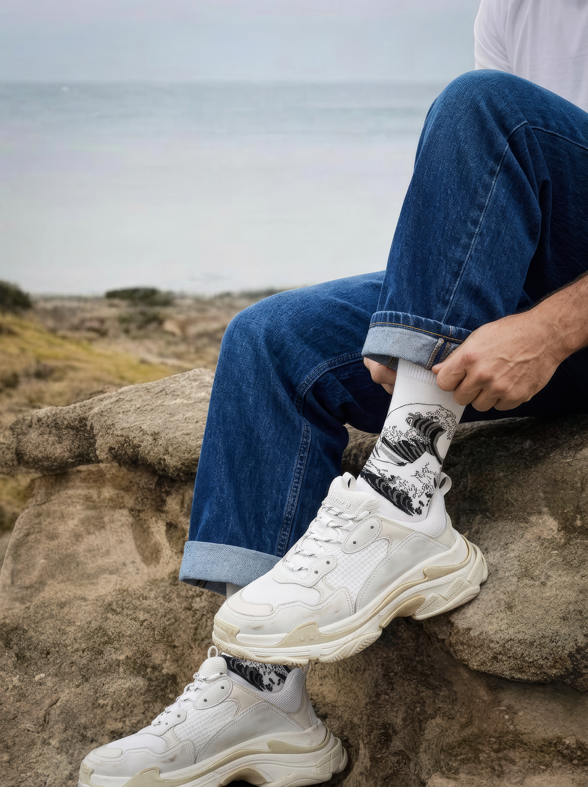 The Great Wave black and white art socks by Katsushika Hokusai worn with white sneakers beside the coast

