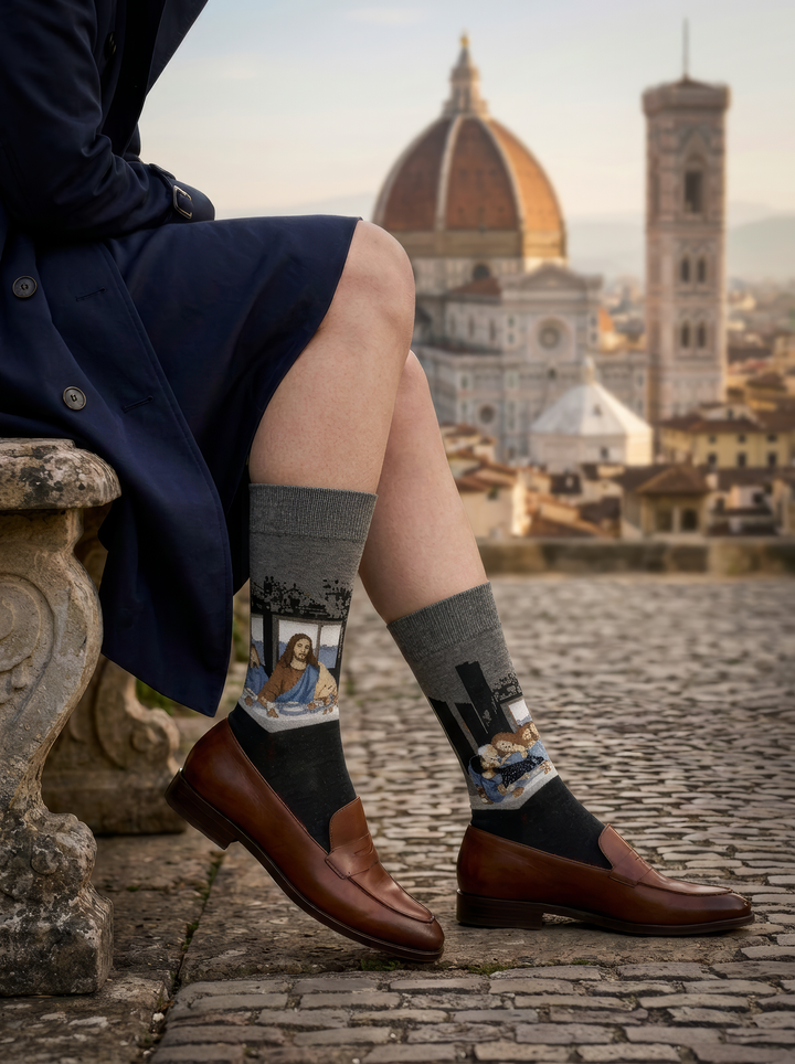 The Last Supper art socks featuring Leonardo da Vinci’s artwork worn with brown leather shoes and blue trousers in a historic city setting