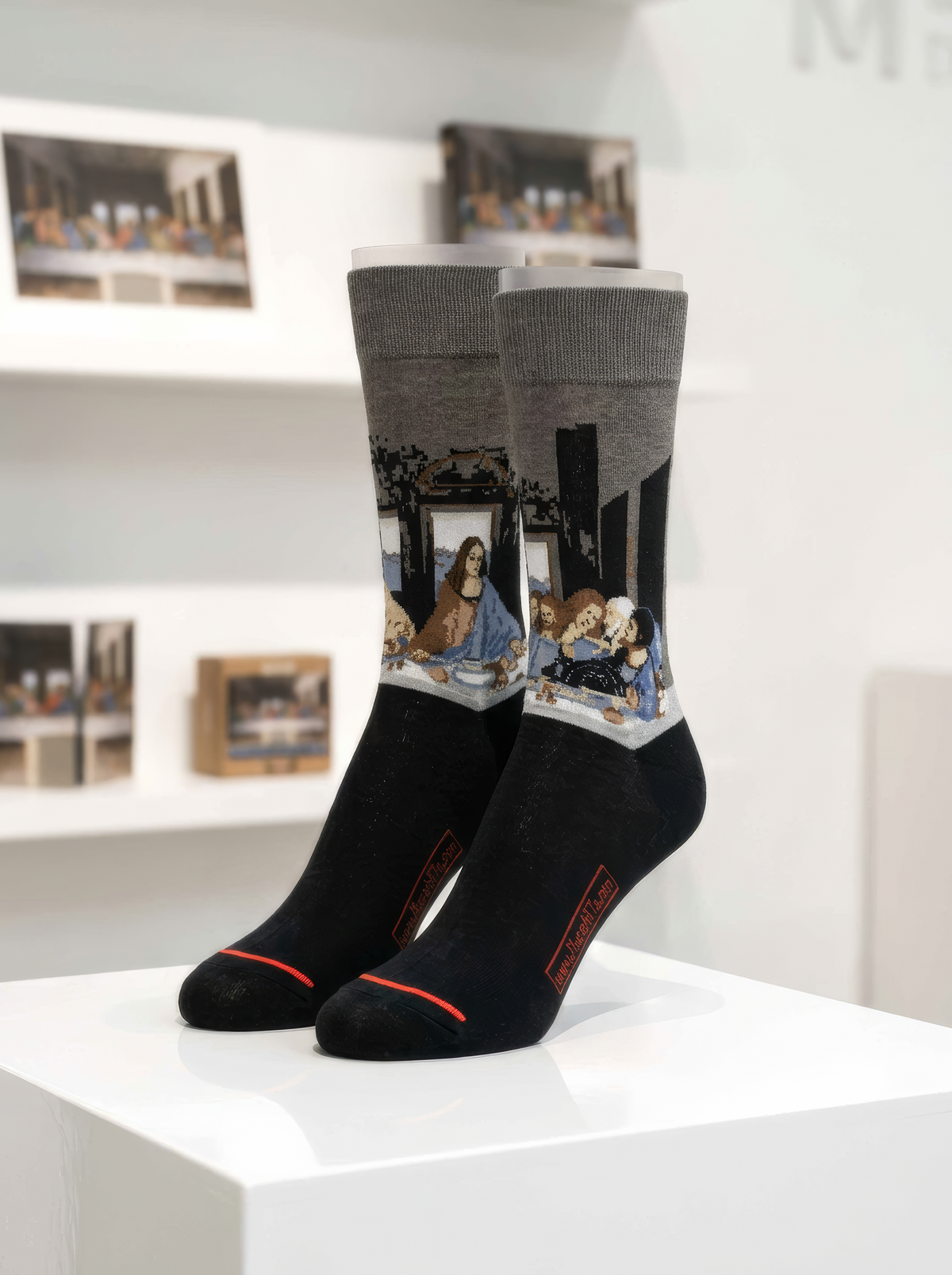 Black and grey The Last Supper art socks featuring Leonardo da Vinci’s artwork displayed on a white pedestal
