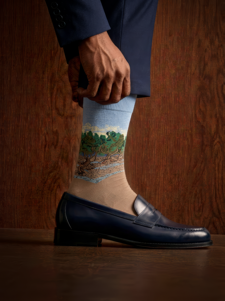 The Olive Trees art socks by Vincent van Gogh worn with a black leather loafer against a wooden background