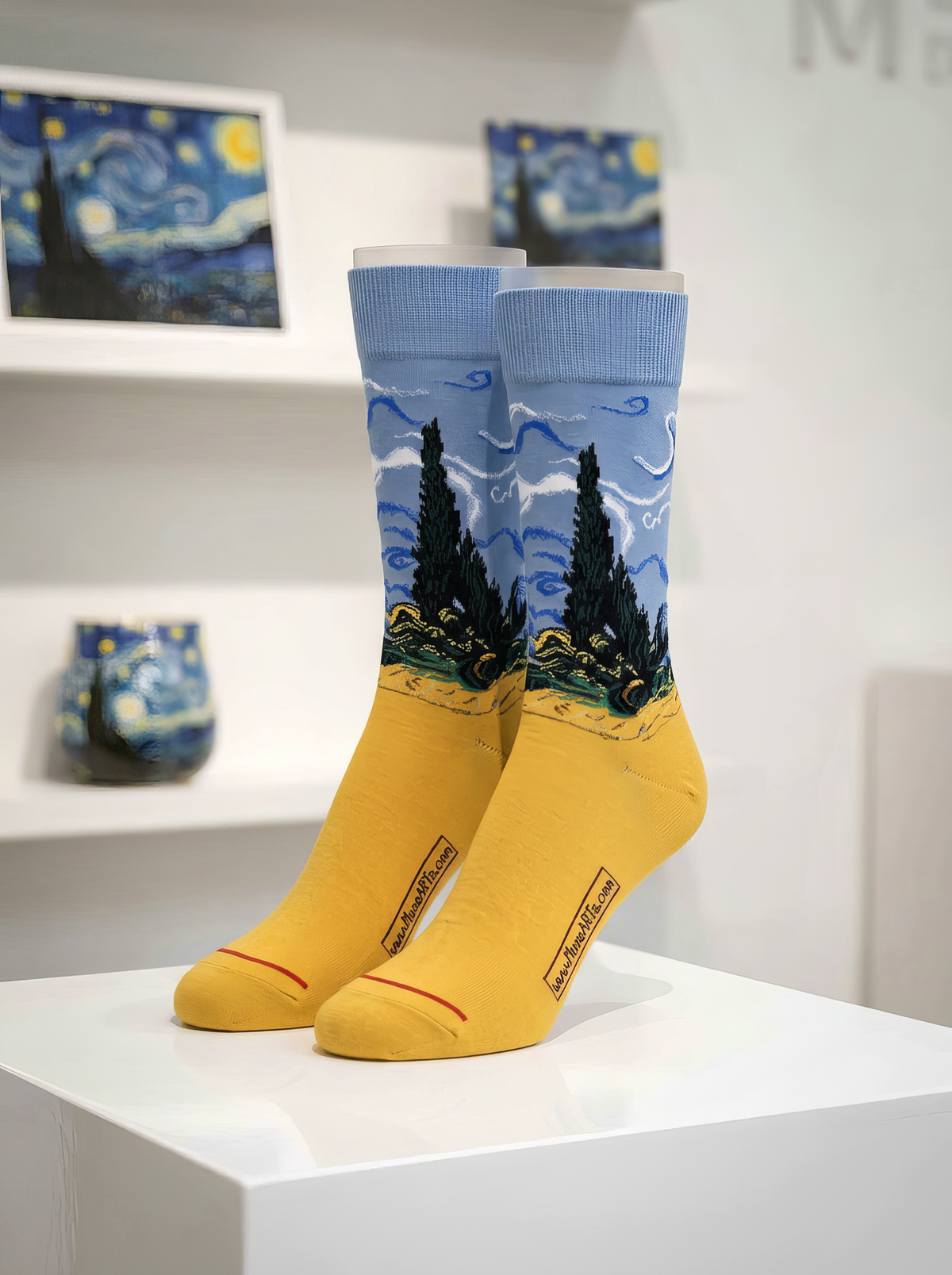 Wheatfield with Cypresses art socks by Vincent van Gogh displayed on a white pedestal in a bright art-filled interior