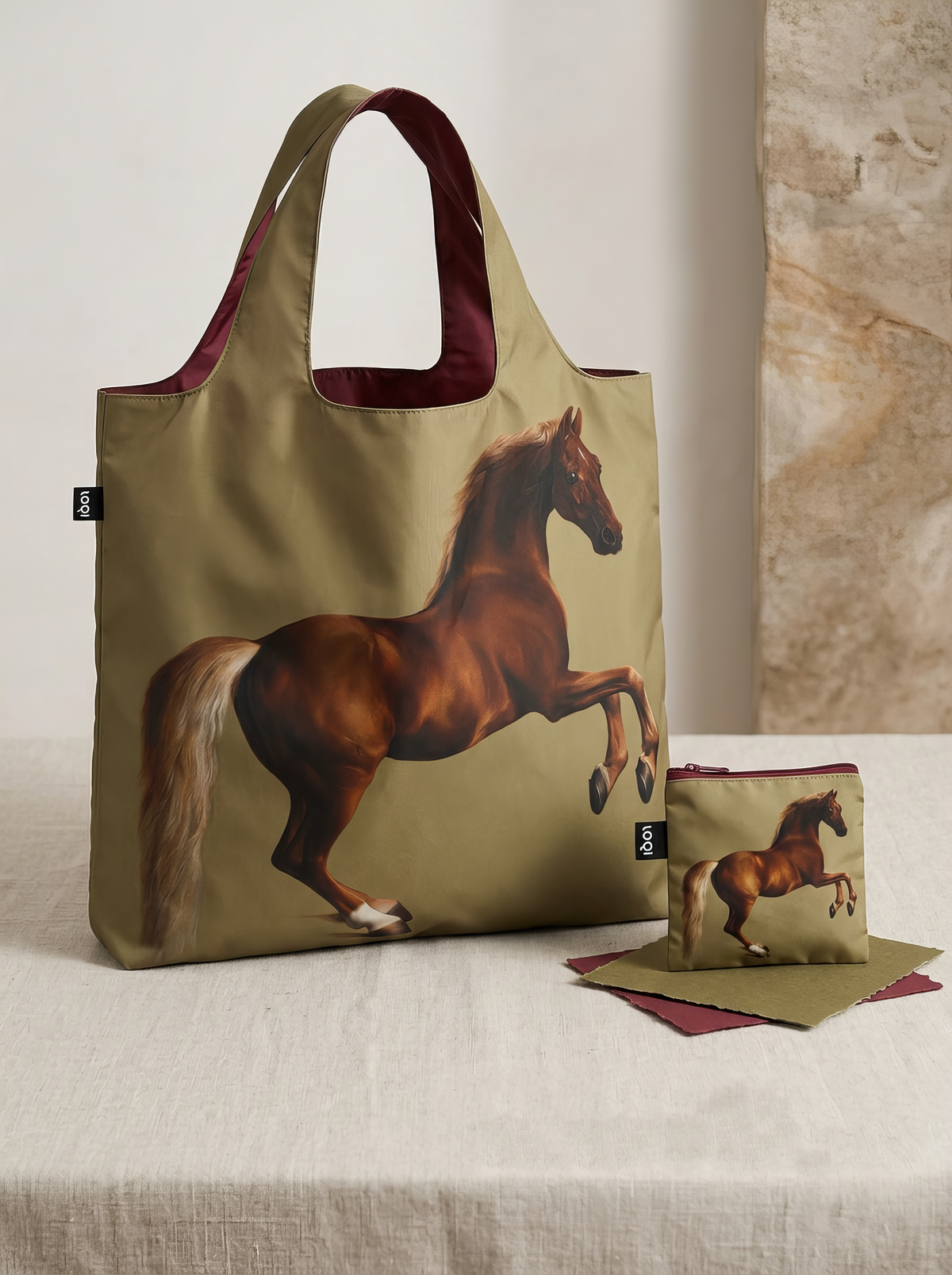 Whistlejacket shopper bag displayed upright beside its matching pouch on a light-coloured pedestal in a softly lit interior.
