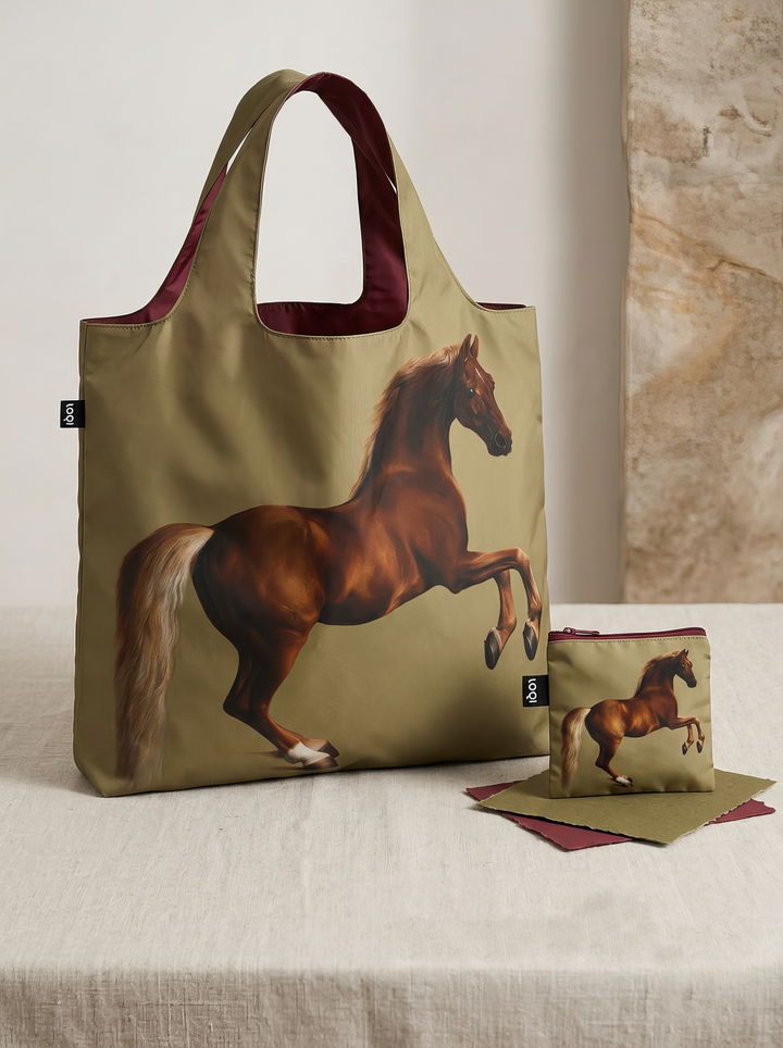 Whistlejacket shopper bag displayed upright beside its matching pouch on a light-coloured pedestal in a softly lit interior.
