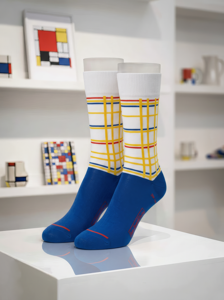 Pair of XL Museum Art Socks featuring Piet Mondrian’s New York City design, displayed on a white pedestal in a gallery setting.⠋

