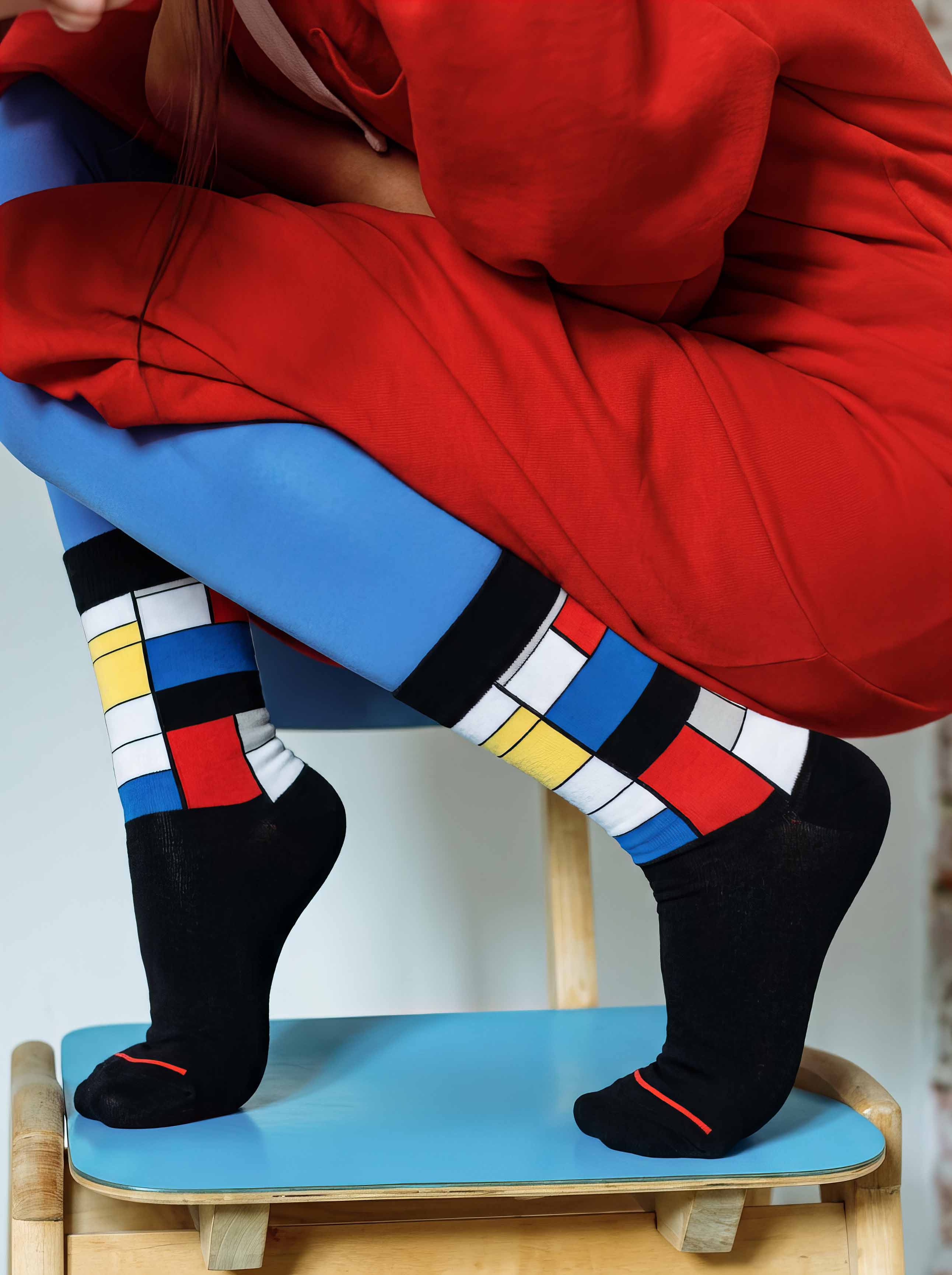 Woman wearing MuseARTa Mondrian art socks with red jacket on skateboard — urban art gift ArtyGifts