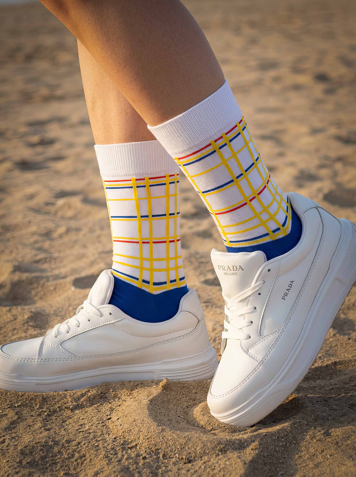 Woman wearing MuseARTa Mondrian New York City art socks with white sneakers on sand — casual De Stijl lifestyle gift ArtyGifts
