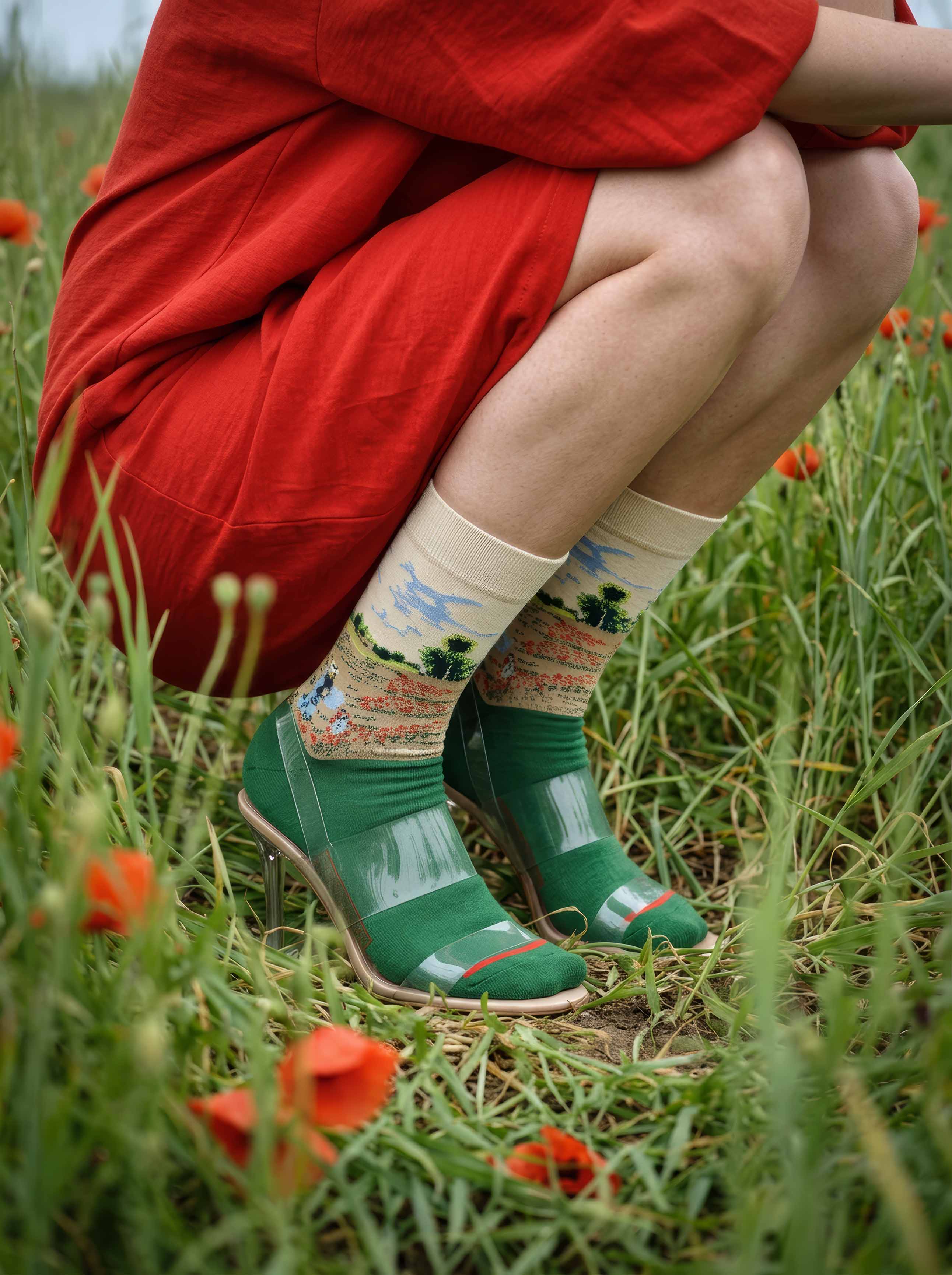 Woman in red dress wearing MuseARTa Monet Field of Poppies art socks crouching in poppy field — Impressionist nature gift ArtyGifts
